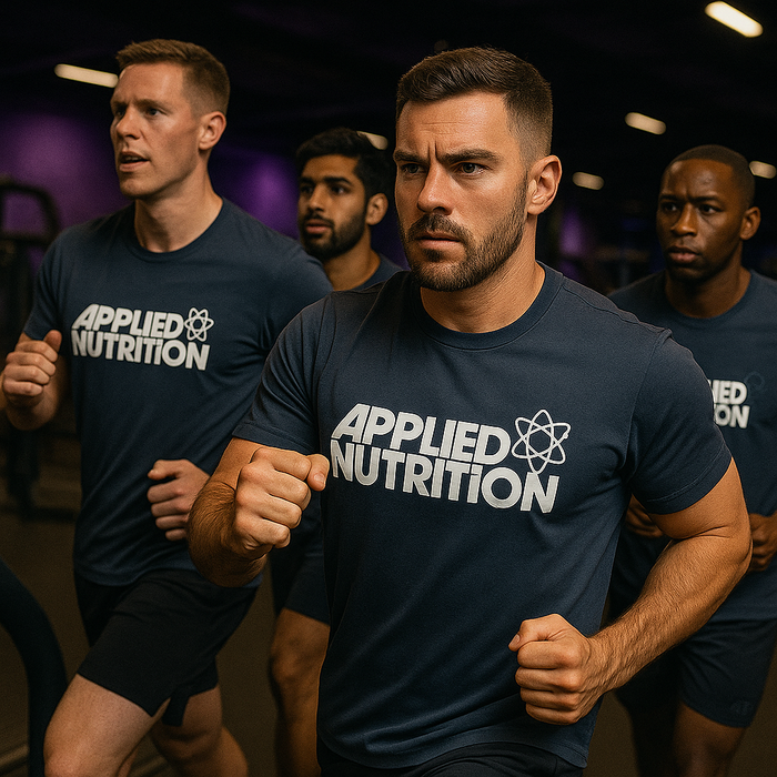 Group of athletic men wearing matching Applied Nutrition t-shirts during a high-intensity interval training session, with subtle MSS purple lighting in the gym background