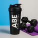 The ABE shaker next to a pair of dumbbells or a yoga mat, condensation droplets on the outside